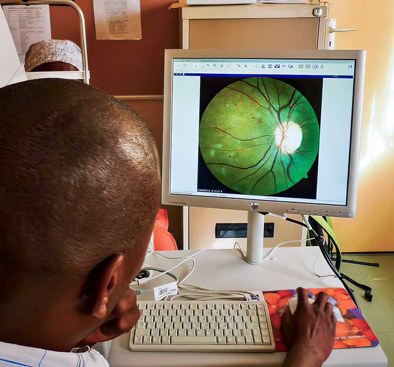 A man sitting at a computer , on the monitor is a retinal image