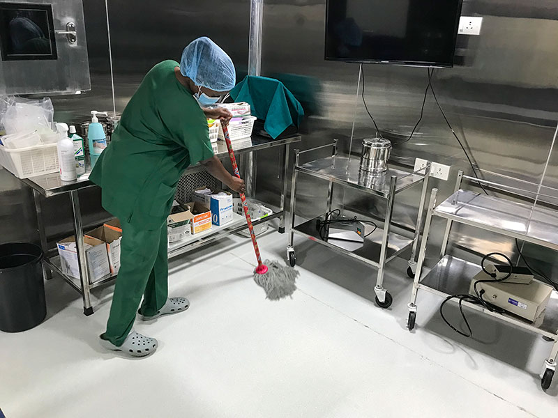 A member of staff wearing green surgical scrubs, a hair net and a mask, mops the operating floor