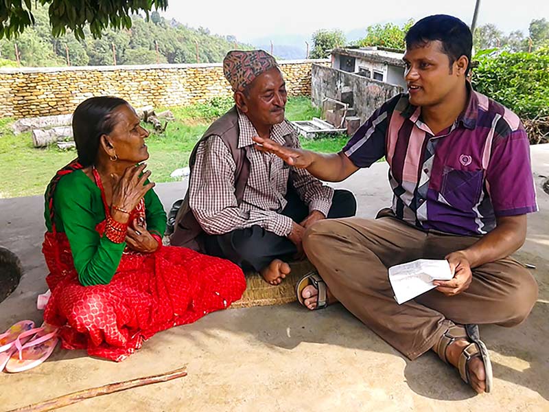 A male counsellor sitting in a village sitting down and talking with a couple