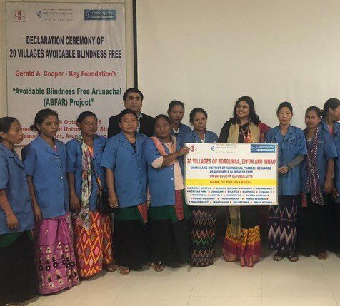 A group of female community health workers grouped for a photo at a training workshop, holding a poster with details of the workshop written on it.