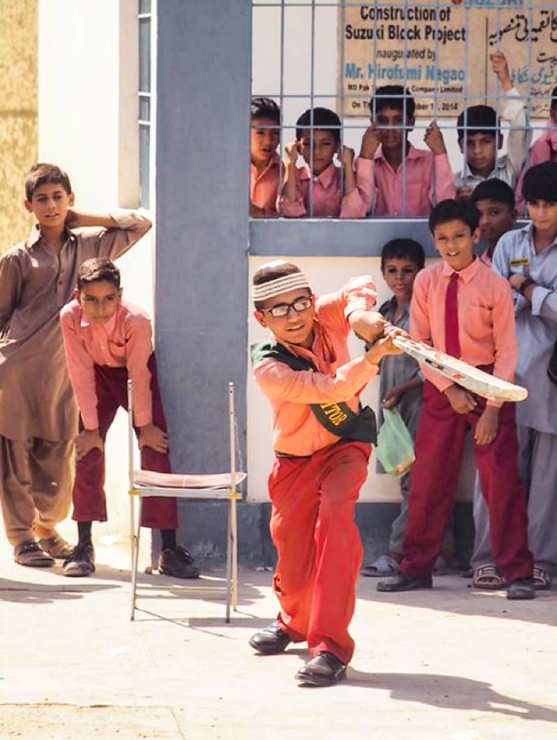 School boy batting during a cricket game at school, watched by other pupils
