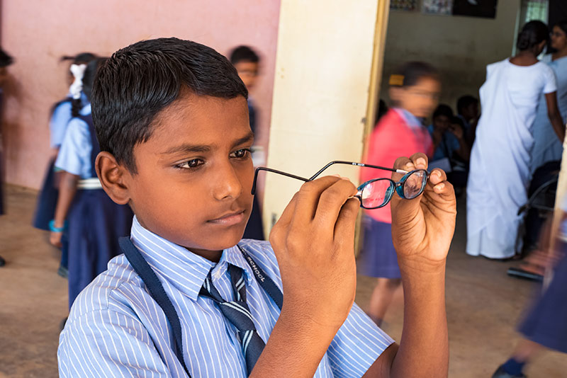 Écolier observant une paire de lunettes qu'il tient dans ses mains.