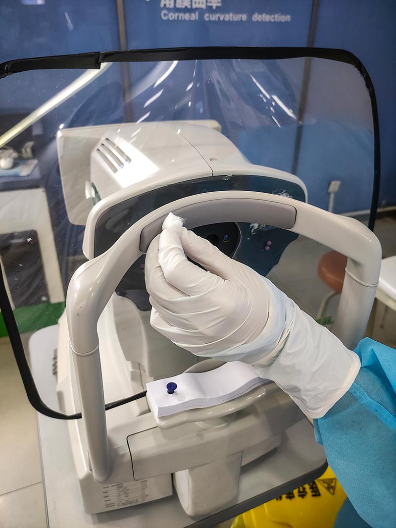 Close up of a health care worker wiping a slit lamp shield using an alcohol wipe