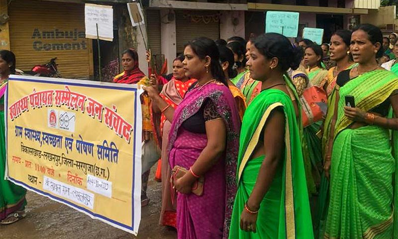 Several female community health workers stand in the street holding placards