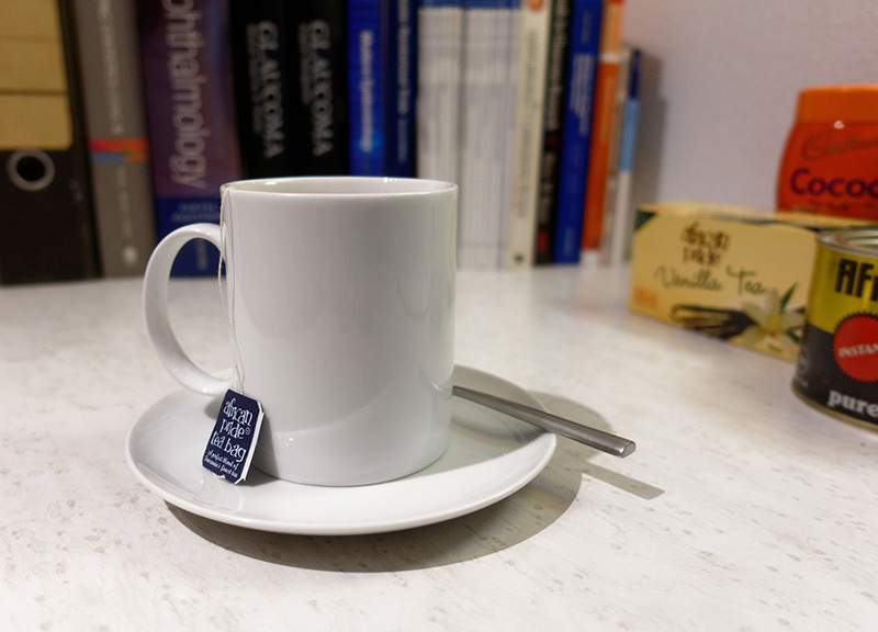 A cup of tea with saucer, tea bag and teaspoon placed on a desk