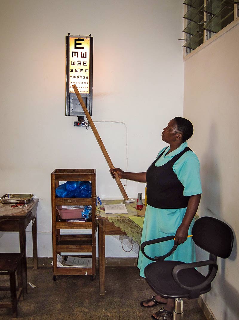 Female ophthalmic staff member pointing to an illuminated tumbling E chart with a wooden pole