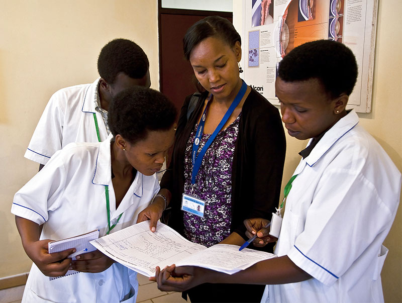 A female ophthalmologist in plain clothes stands holding a book with three healthcare staff dressed in white uniforms.