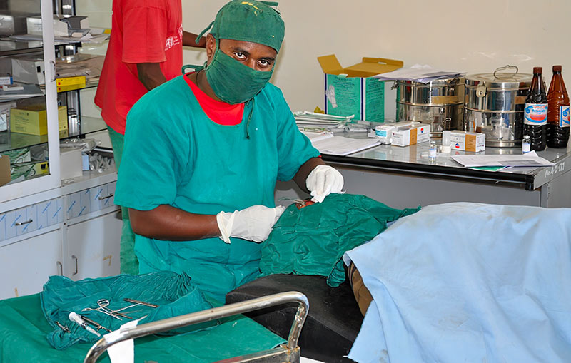 Ophthalmic staff member dressed in surgical greens performing eye surgery on a patient whose face is covered with a green drape