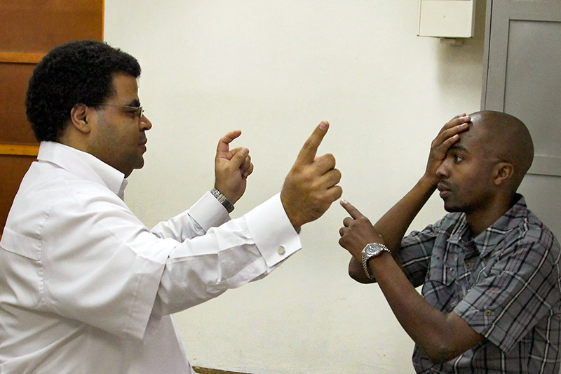 Optometrist holding up two fingers, one on each hand and patient covering one eye and pointing to the left hand of the examiner