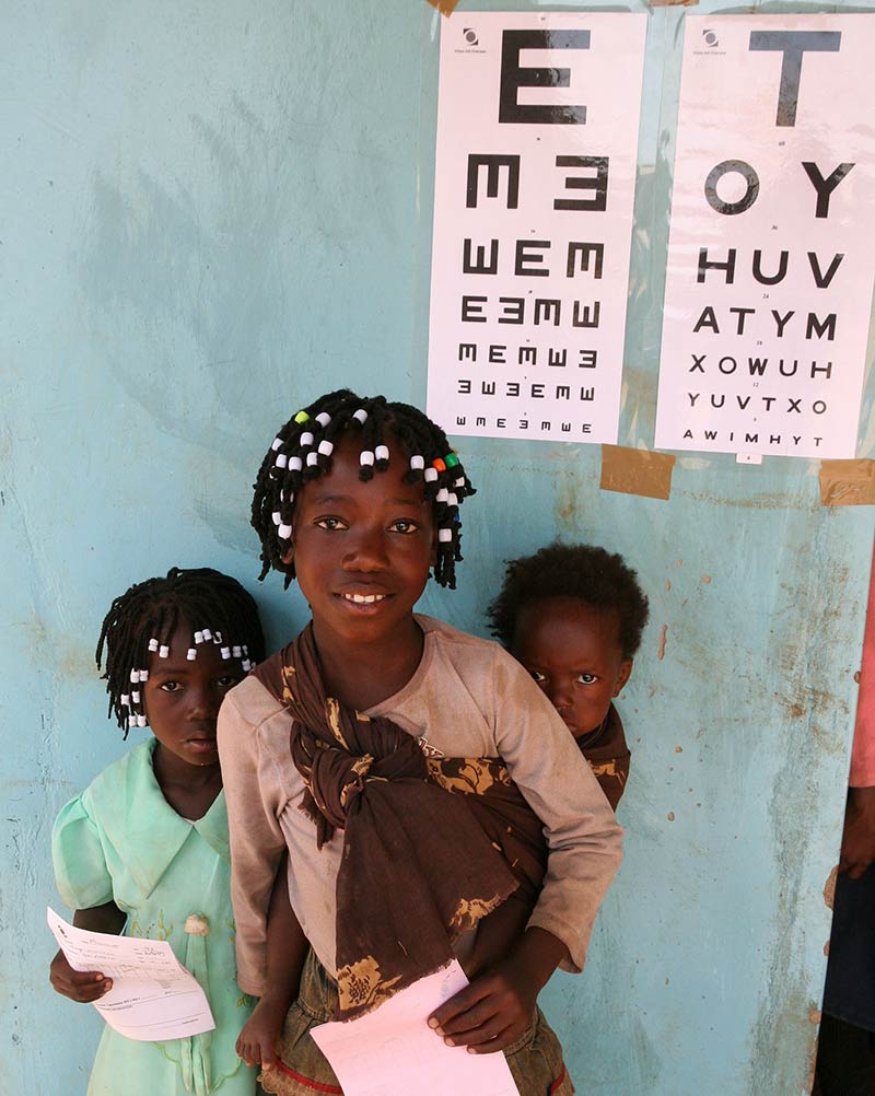 Young girls standing underneath a Tumbling E and a Snellen chart on a wall