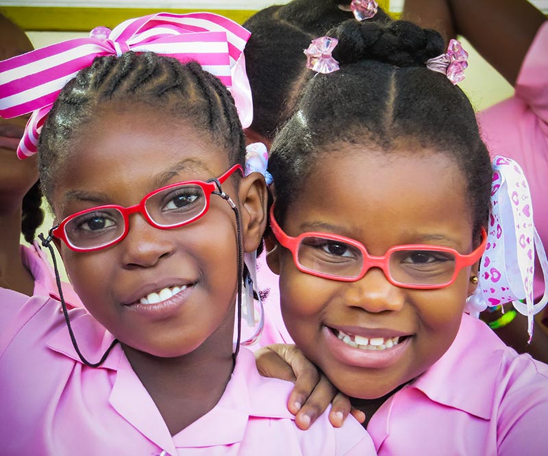 Deux écolières souriantes ; toutes deux portent des lunettes.