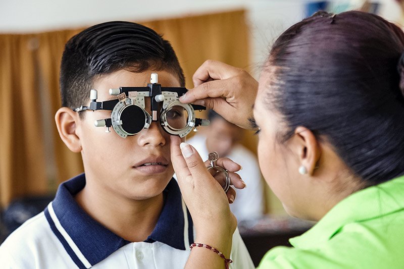 Garçon portant une monture d'essai pendant qu'une optométriste réalise les ajustements nécessaires.