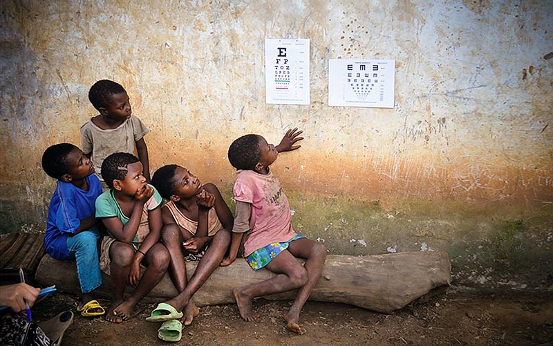 Five African children looking at a Snellen chart on the wall of a house
