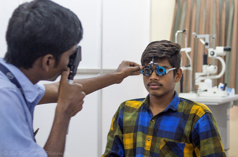 Patient wearing refracting spectacles and an optometrist holding a direct ophthalmoscope