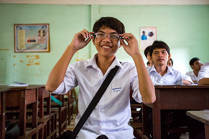 Boy trying spectacles in a classroom and smiling