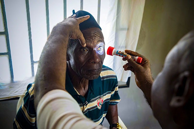 A primary care worker shines a torch into the right eye of a patient, while steadying their head using his left hand