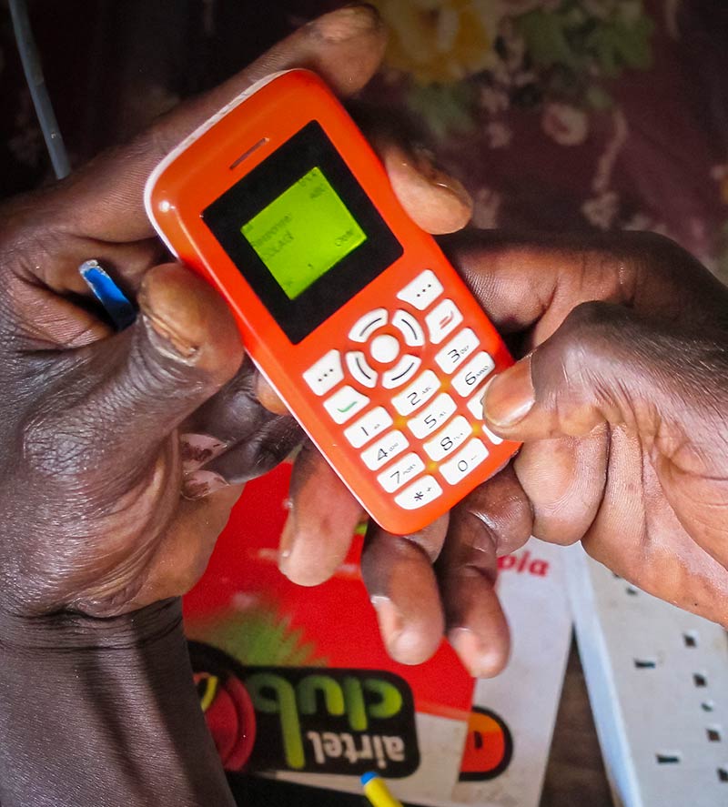 An orange mobile phone in a Zambian women's hands. She is entering a telephone number/message