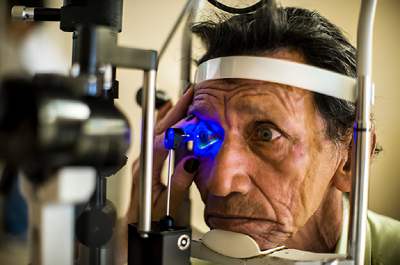 A gentleman having his right eye examined at the slit lamp with a blue light. He has his chin on the rest.