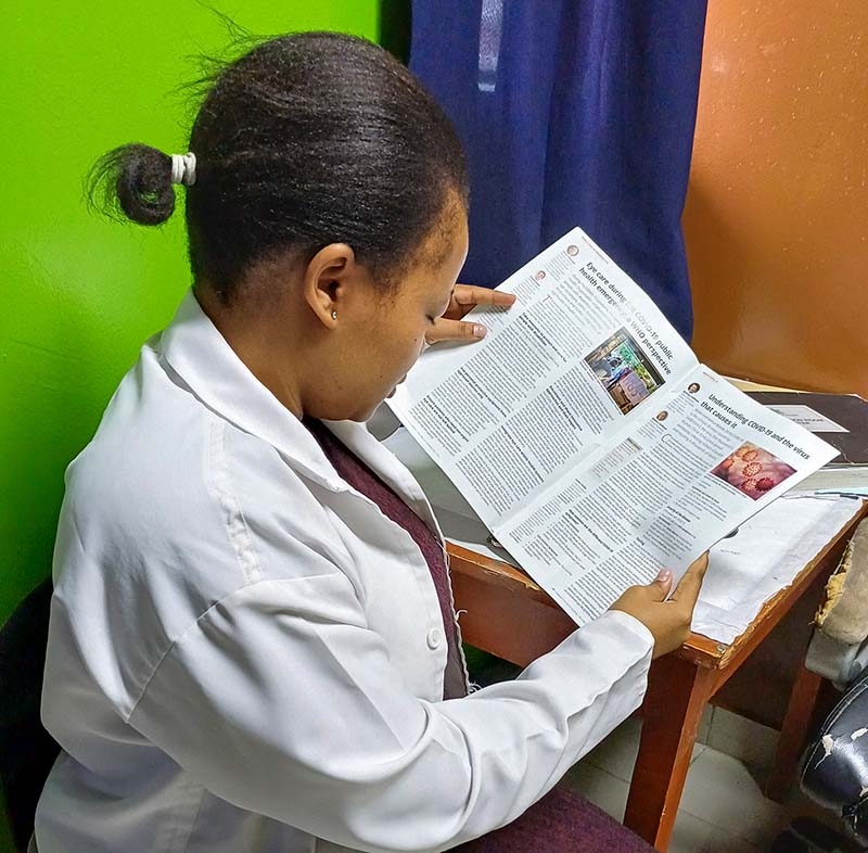 A female eye care worker is sitting at a desk reading a copy of the journal.